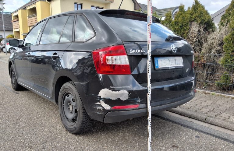 Schwarz-matter Kombi mit beschädigter Heckstoßstange auf einer Straße geparkt.